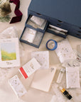 Contents of the Tom’s Studio Advent Calendar displayed on a table: wrapped gifts, mini ink bottles, washi tape, a notebook, and other stationery items, with the drawer box in the background.
filter_alt_text
