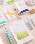 A close-up of unwrapped advent calendar gifts from Tom’s Studio, including mini ink samples, a pen, notebooks, and accessories, styled on a cream fabric background. filter_alt_text