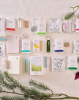 The full contents of the Tom’s Studio advent calendar laid out, including pens, ink samples, notebooks, tea sachets, and stationery accessories, styled with festive greenery and ribbon. filter_alt_text