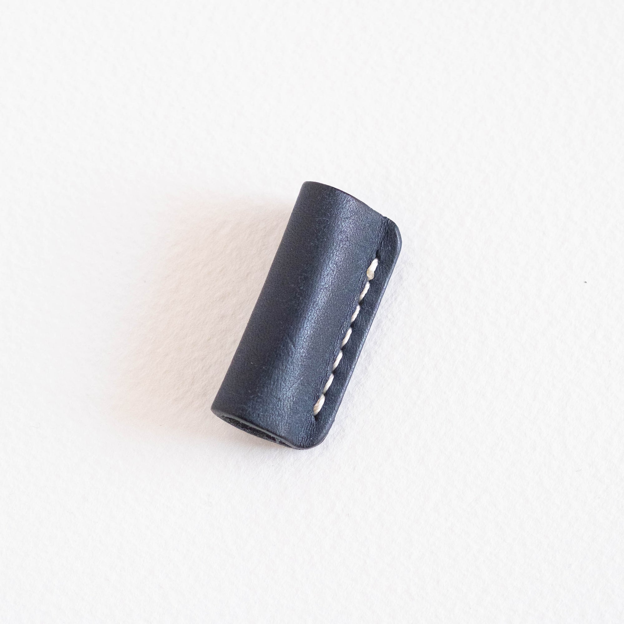 Midnight leather grip and rollstop for the Lumos pen, lying flat with visible white stitching on a clean white surface.