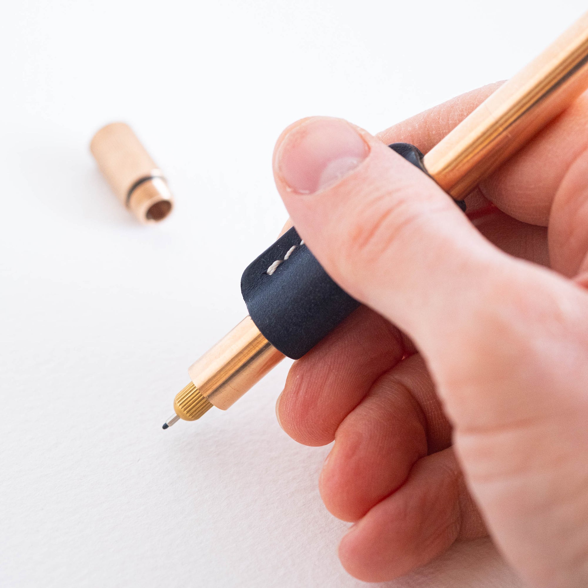 Close-up of a hand holding the Lumos Pro in Bronze, fitted with the Midnight leather grip and rollstop.