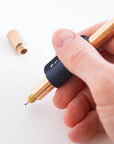 Close-up of a hand holding the Lumos Pro in Bronze, fitted with the Midnight leather grip and rollstop.