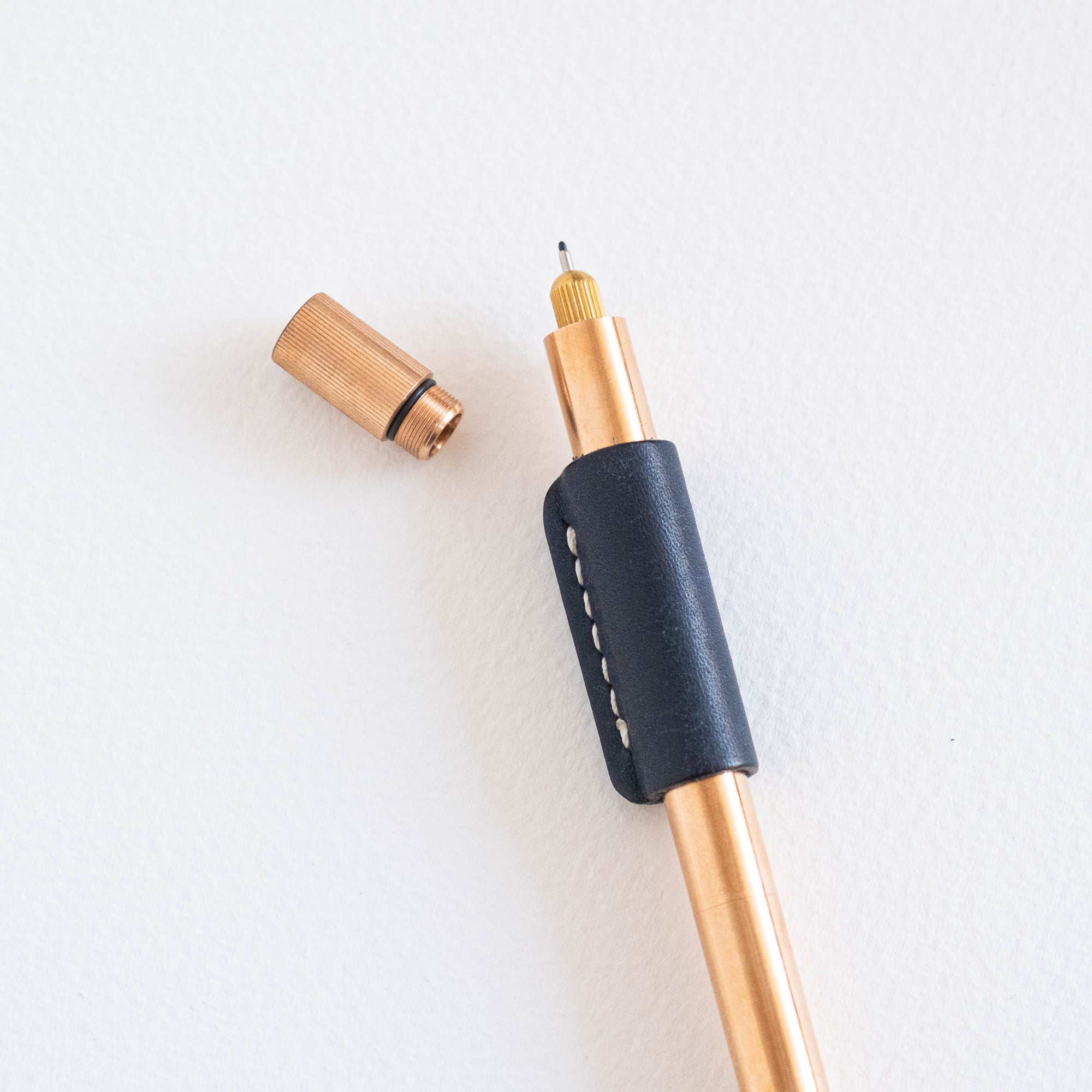 Bronze Lumos Pro pen with Midnight leather grip and rollstop fitted; cap placed beside on a white background.
