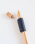 Bronze Lumos Pro pen with Midnight leather grip and rollstop fitted; cap placed beside on a white background.