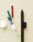 A Matte Black Lumos Duo and a Reservoir and Tip Container displayed on a light beige coloured background. The container has it's lid off and 3 ink reservoirs are coming out of the container that are colours with red, green and blue ink.