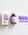 Tom's Studio Lavender Fountain Pen Ink – bottle with gold lid, boxed packaging featuring a purple and gold label marked '22', and a swatch of the vibrant lavender ink on textured paper.
