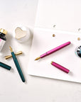 Zoom fountain pen nib fitted in the Studio Fountain Pen in Ivy, and Fude fountain pen nib fitted in the Studio Fountain Pen in Mulberry, pictured with ink and accessories
