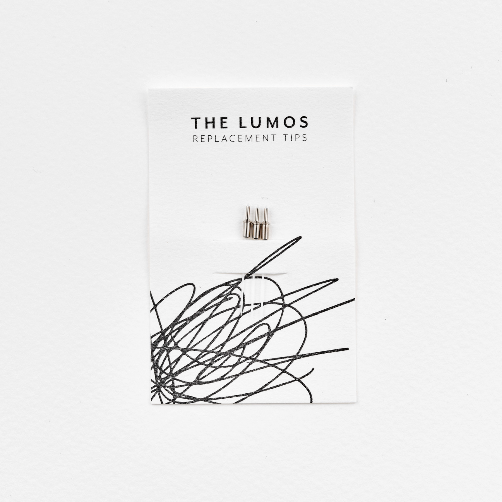 A pack of three Lumos 0.2mm fineliner replacement tips attached to a white backing card. The card features 'THE LUMOS REPLACEMENT TIPS' in uppercase black letters at the top, with an abstract black ink scribble design in the lower half. A black textured label in the upper right corner displays '0.2 Fineliner Tip' in white text.