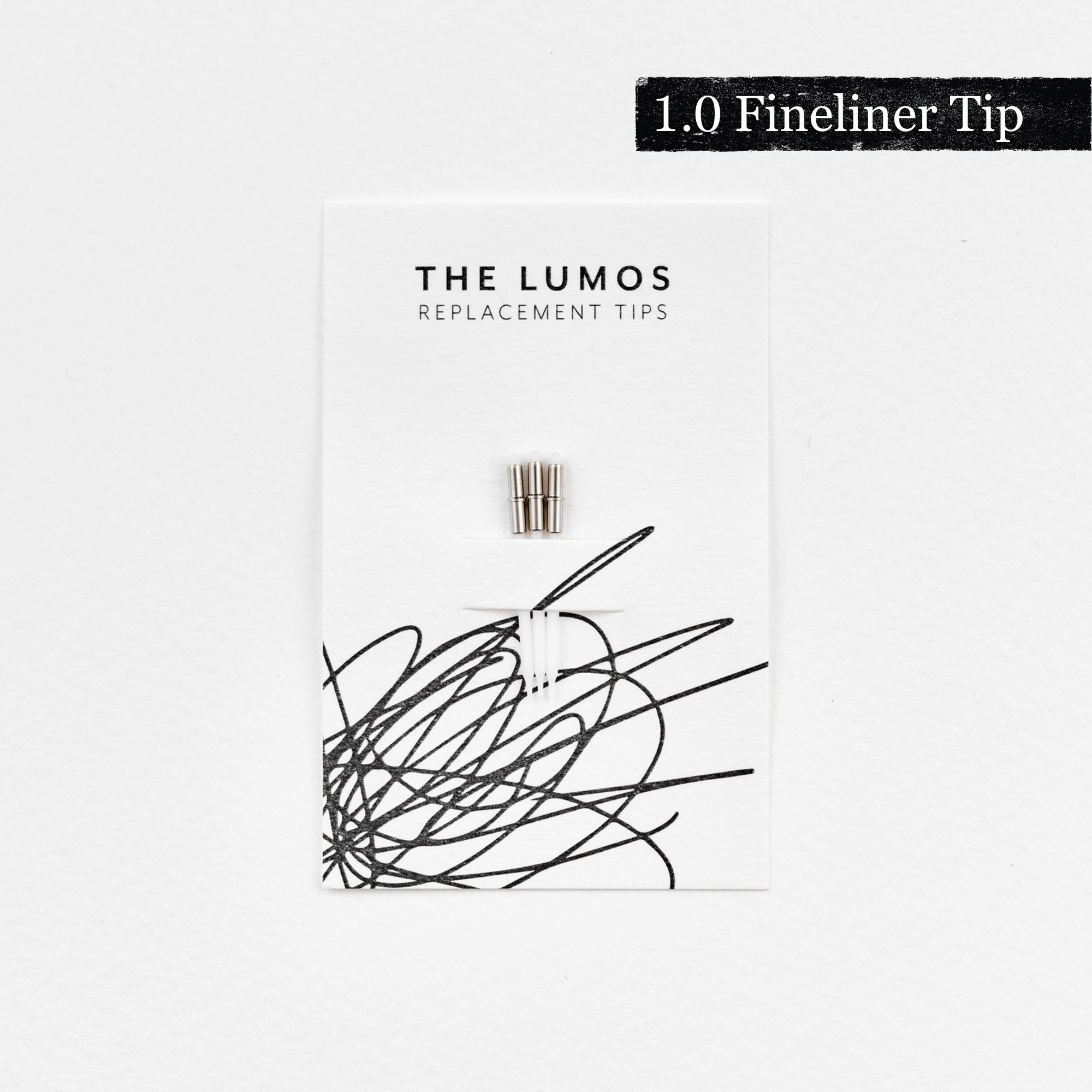 A pack of three Lumos 1.0mm fineliner replacement tips attached to a white backing card. The card features 'THE LUMOS REPLACEMENT TIPS' in uppercase black letters at the top, with an abstract black ink scribble design in the lower half. A black textured label in the upper right corner displays '1.0 Fineliner Tip' in white text.