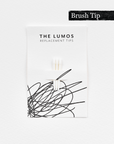 A pack of three Lumos replacement Brush tips attached to a white backing card. The card features 'THE LUMOS REPLACEMENT TIPS' in uppercase black letters at the top, with an abstract black ink scribble design in the lower half. A black textured label in the upper right corner displays 'Brush Tip' in white text.