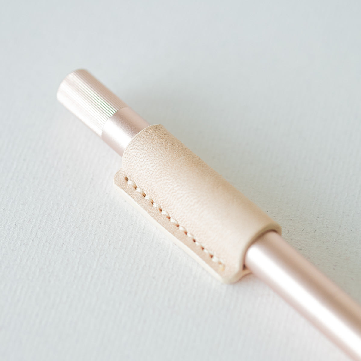 Handmade by Edward De Lacy, a leather pen grip and rollstop for the Lumos refillable pen – shown in natural leather on the rose gold Lumos