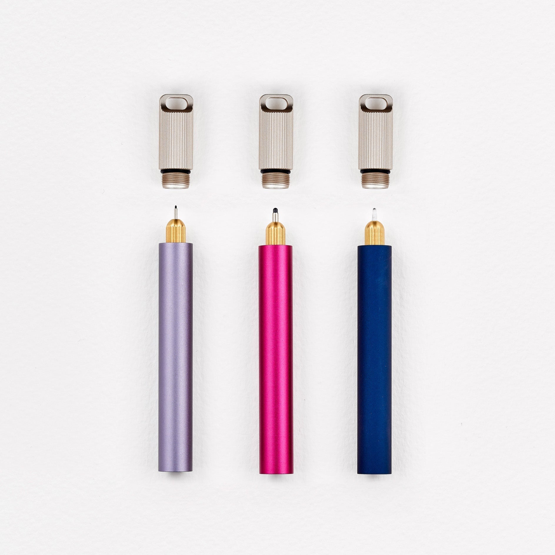 A display of three Lumos Mini pens with their Lumos Loop Lids removed, showing the internal interchangeable tips. The components are arranged to highlight their modular and customizable design.