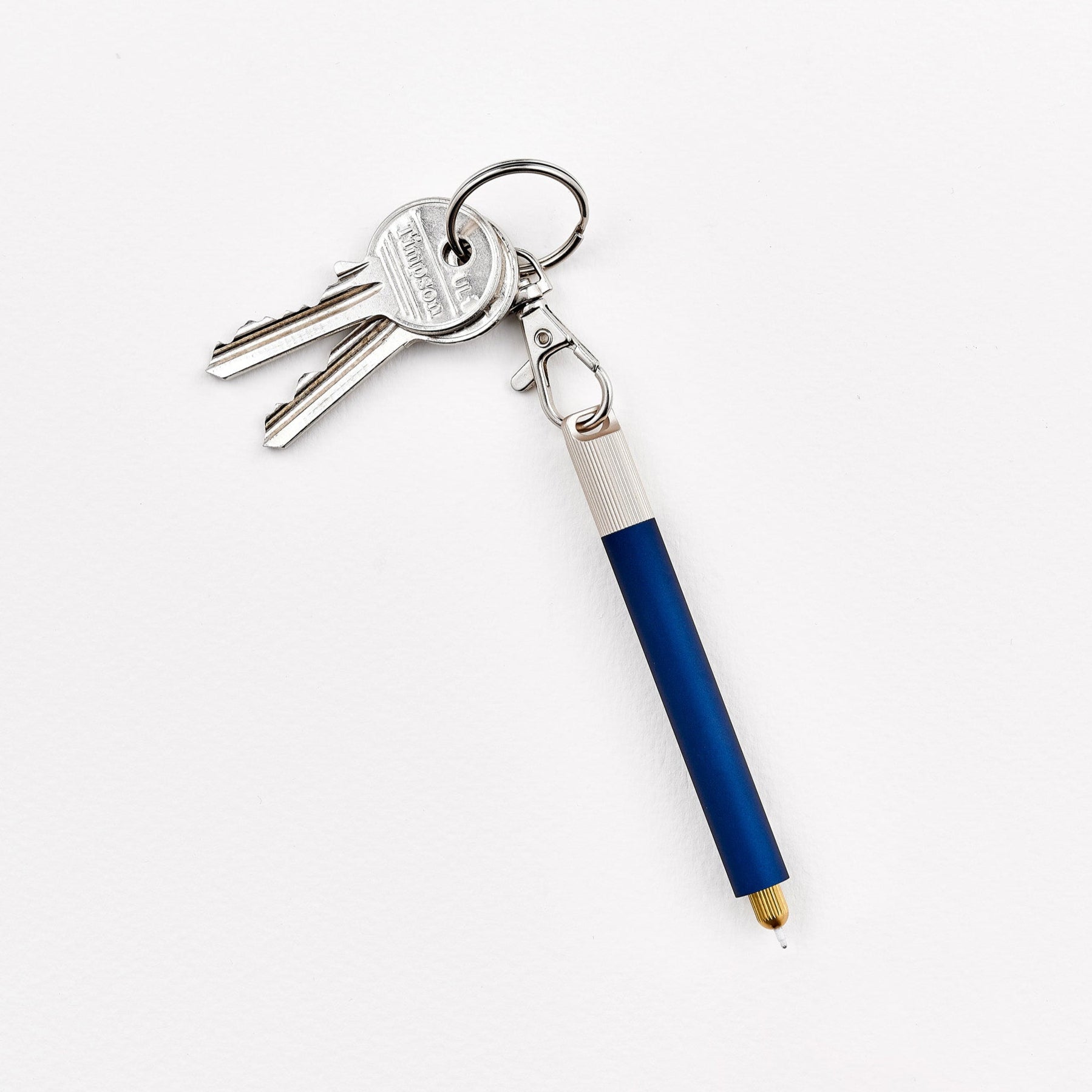 A close-up of a Lumos Loop Lid attached to a Midnight Lumos Mini pen, clipped onto a keyring. The cap is slightly open, showing the interchangeable writing tip.