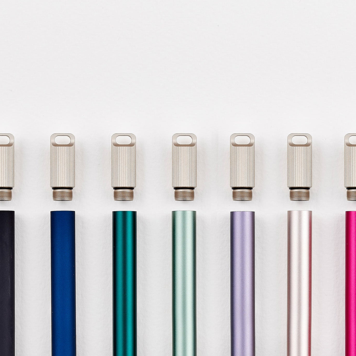 A lineup of multiple Lumos Mini pens in a variety of colours each pictured with a Lumos Loop Lid, arranged neatly in a row on a white background.