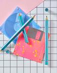 Close-up of Lumos Splash pens in Blue Raspberry colourway with pink splatter, styled with neon pink and blue floppy disks on a grid background.