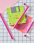 Close-up of Lumos Splash pens in Bubblegum pink with blue splatter, styled with neon green and pink floppy disks on a grid background.