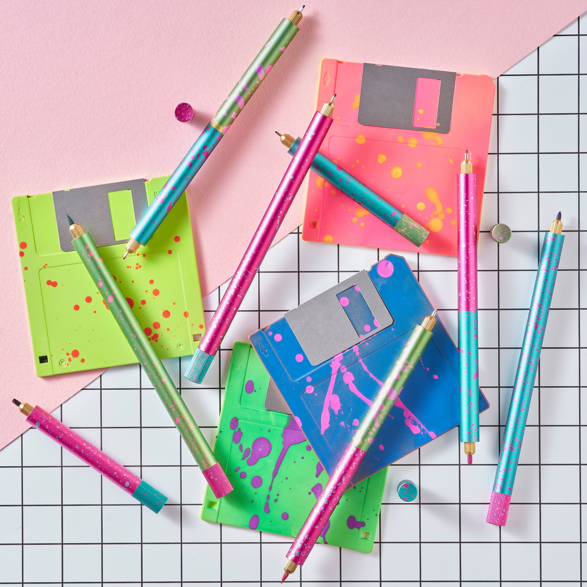 Flat lay of Lumos Splash pens in neon Appletini, Blue Raspberry, and Bubblegum colourways, styled with colourful floppy disks on a grid background.