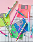 Flat lay of Lumos Splash pens in neon Appletini, Blue Raspberry, and Bubblegum colourways, styled with colourful floppy disks on a grid background.