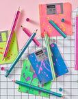 Flat lay of Lumos Splash pens in all three neon colourways with paint-splatter patterns, arranged with bright floppy disks on a grid background.