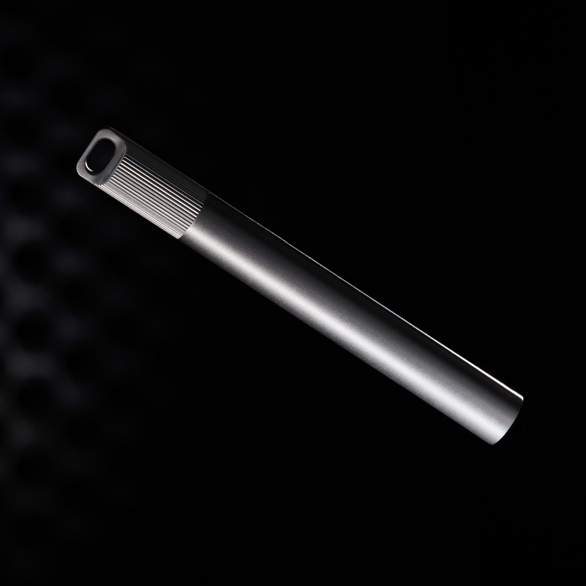 Titanium Lumos Mini shown capped, with the loop lid in focus and the pen’s minimalist silhouette catching a soft metallic glow.