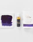 A mini ink sample bottle of Constellation purple fountain pen ink by Tom’s Studio, displayed alongside a swatch of the ink on textured paper and its matching packaging. The bottle is small, with a gold cap and a white pipette dropper, and features 'Tom’s Studio' in gold lettering. The ink swatch shows a rich, shimmering hue with a gradient from deep to lighter tones. The packaging, a small white card, has 'Tom’s Studio' embossed in gold at the top, with a brushstroke of the ink colour at the bottom.