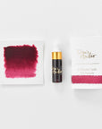 A mini ink sample bottle of Mulberry red fountain pen ink by Tom’s Studio, displayed alongside a swatch of the ink on textured paper and its matching packaging. The bottle is small, with a gold cap and a white pipette dropper, and features 'Tom’s Studio' in gold lettering. The ink swatch shows a rich, shimmering hue with a gradient from deep to lighter tones. The packaging, a small white card, has 'Tom’s Studio' embossed in gold at the top, with a brushstroke of the ink colour at the bottom.
