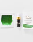 A mini ink sample bottle of New Forest Green fountain pen ink by Tom’s Studio, displayed alongside a swatch of the ink on textured paper and its matching packaging. The bottle is small, with a gold cap and a white pipette dropper, and features 'Tom’s Studio' in gold lettering. The ink swatch shows a rich, shimmering hue with a gradient from deep to lighter tones. The packaging, a small white card, has 'Tom’s Studio' embossed in gold at the top, with a brushstroke of the ink colour at the bottom.