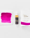 A mini ink sample bottle of Raspberry Sorbet pink fountain pen ink by Tom’s Studio, displayed alongside a swatch of the ink on textured paper and its matching packaging. The bottle is small, with a gold cap and a white pipette dropper, and features 'Tom’s Studio' in gold lettering. The ink swatch shows a rich, shimmering hue with a gradient from deep to lighter tones. The packaging, a small white card, has 'Tom’s Studio' embossed in gold at the top, with a brushstroke of the ink colour at the bottom.
