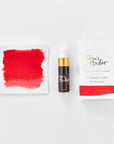 A mini ink sample bottle of Strawberry Jam red fountain pen ink by Tom’s Studio, displayed alongside a swatch of the ink on textured paper and its matching packaging. The bottle is small, with a gold cap and a white pipette dropper, and features 'Tom’s Studio' in gold lettering. The ink swatch shows a rich, shimmering hue with a gradient from deep to lighter tones. The packaging, a small white card, has 'Tom’s Studio' embossed in gold at the top, with a brushstroke of the ink colour at the bottom.