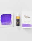 A mini ink sample bottle of Amethyst purple shimmer fountain pen ink by Tom’s Studio, displayed alongside a swatch of the ink on textured paper and its matching packaging. The bottle is small, with a gold cap and a white pipette dropper, and features 'Tom’s Studio' in gold lettering. The ink swatch shows a rich, shimmering hue with a gradient from deep to lighter tones. The packaging, a small white card, has 'Tom’s Studio' embossed in gold at the top, with a brushstroke of the ink colour at the bottom.