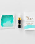 A mini ink sample bottle of Barrier Reef blue shimmer fountain pen ink by Tom’s Studio, displayed alongside a swatch of the ink on textured paper and its matching packaging. The bottle is small, with a gold cap and a white pipette dropper, and features 'Tom’s Studio' in gold lettering. The ink swatch shows a rich, shimmering hue with a gradient from deep to lighter tones. The packaging, a small white card, has 'Tom’s Studio' embossed in gold at the top, with a brushstroke of the ink colour at the bottom.