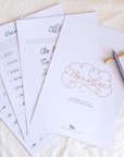 Flat-lay of several pages from the Monoline Lettering Guide, including the cover page, warm-up strokes, alphabet guides, and connecting letters. A lilac-coloured Lumos pen with brass butterfly pen rest is placed on top.