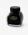 A bottle of Platinum Carbon Ink is positioned at a slight angle, showing the left side of the bottle. The ink is housed in a uniquely shaped glass bottle with a black screw-on lid. The label is gold and black, featuring the words "Carbon Ink" prominently in the centre.