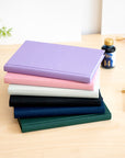 A stack of vibrant Semikolon A5 notebooks in various colours, with premium linen bound covers, displayed alongside drawing tools and ink.