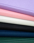 Detail of the embossed spine logo on a stack of vibrant Semikolon A5 notebooks in various colours, including Lilac, Flamingo pink, Moss green, Black, Marine blue and Forest green, with premium linen bound covers.