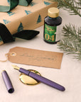 Contents of the Studio Fountain Pen Gift Set including Studio Fountain pen in Iris with Medium Gold nib, New Forest Green Fountain Pen Ink and Solid Brass Pen Rest.