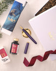 Contents of the Studio Fountain Pen Gift Set including Studio Fountain pen in Iris with Medium Gold nib, Mulberry Fountain Pen Ink and Solid Brass Pen Rest.