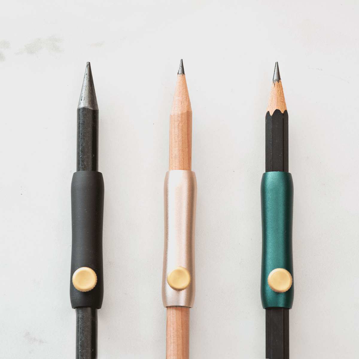 The Poise Pencil Grip Extender in (left to right) Black, Blush and Ivy. Shown on a standard pencil.