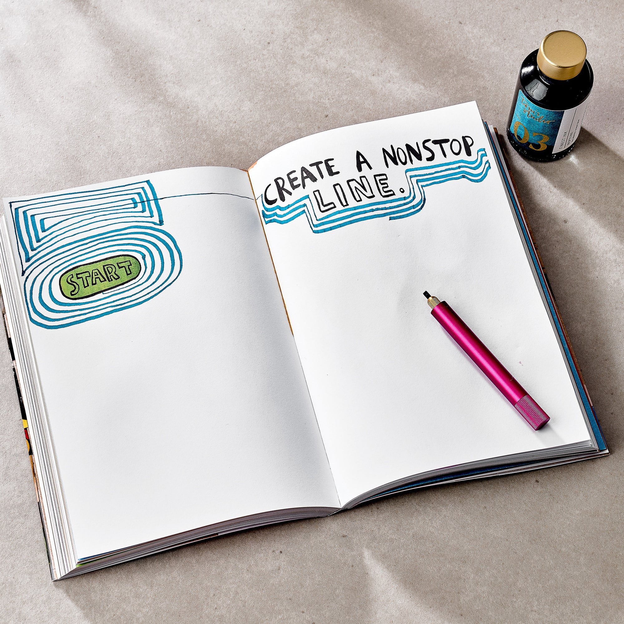 A different spread from Wreck This Journal, showing a creative drawing prompt. The left page displays layered blue and green lines encircling the word “START.” The right page contains the instruction: “CREATE A NONSTOP LINE.” with blue wavy lines drawn underneath. A pink drawing pen and a single bottle of blue-labelled ink rest beside the journal.