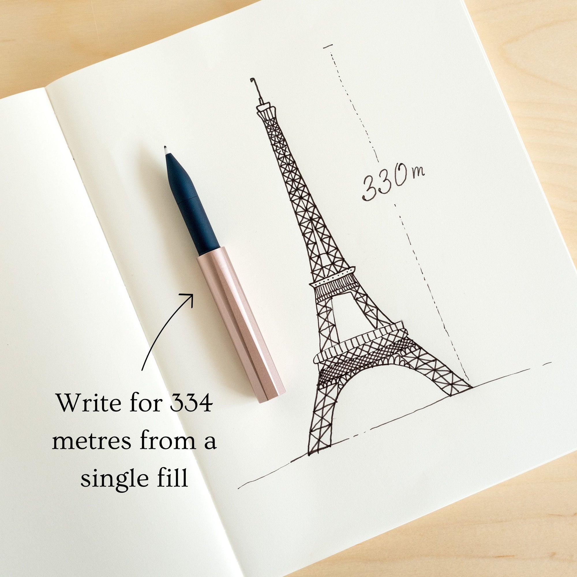 The Wren refillable everyday writing pen in Blush (lid) and Midnight (body) shown on an open notebook explaining that a single reservoir fill will write for 334 metres (the height of the Eiffel Tower)