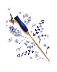 The Bloom calligraphy pen with oblique nib setting in Bluebell on a background of illustrations in ink