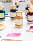 A selection of Tom's Studio Calligraphy inks on a desk with swatches showing their colours on the tabletop