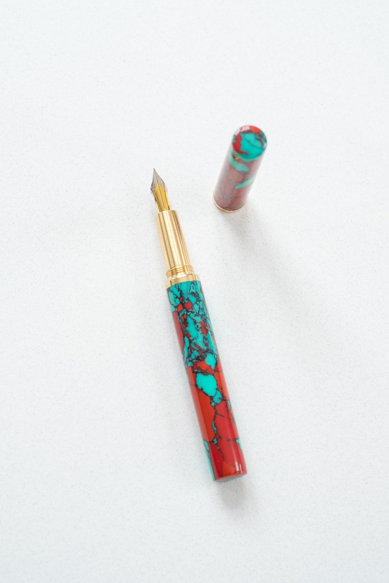 A red jasper Studio pen on a white desk with a flexible fountain pen nib