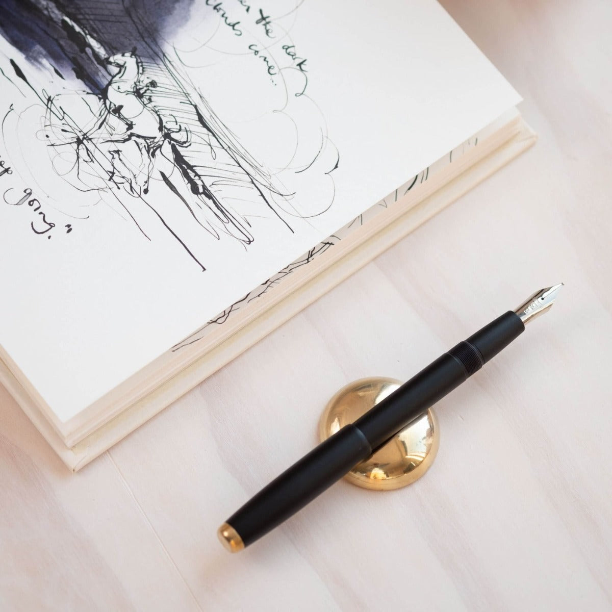 The Studio Fountain Pen in Black shown on the Solid Brass Pen Rest.