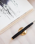 The Studio Fountain Pen in Black shown on the Solid Brass Pen Rest.