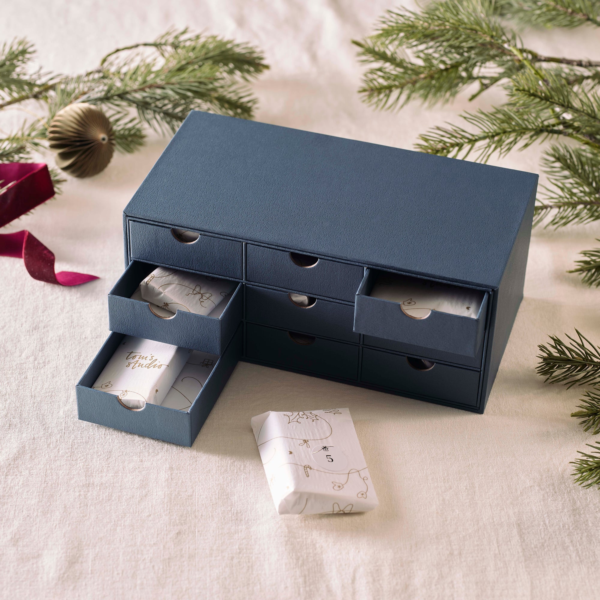 Close-up of the Tom’s Studio Advent Calendar drawers partially open, revealing wrapped gifts inside with gold festive illustrations.