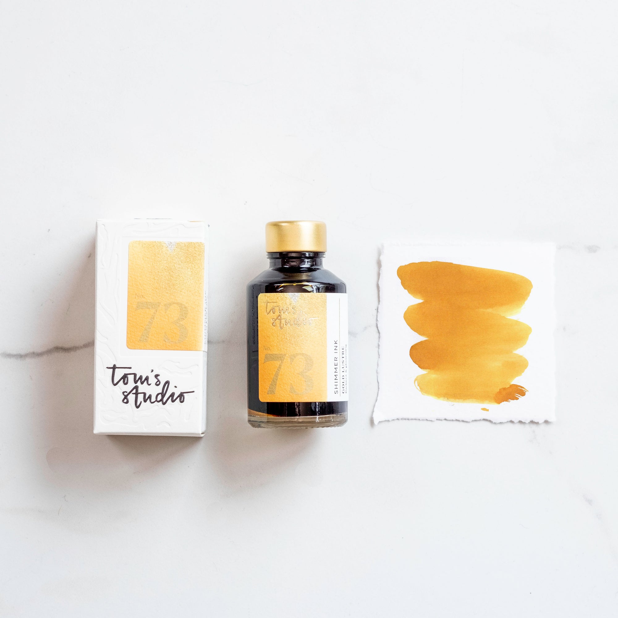 Tom's Studio Golden Lustre Shimmer Fountain Pen Ink with two pens with inky goodness on paper with an ink swatch demonstrating the colour
