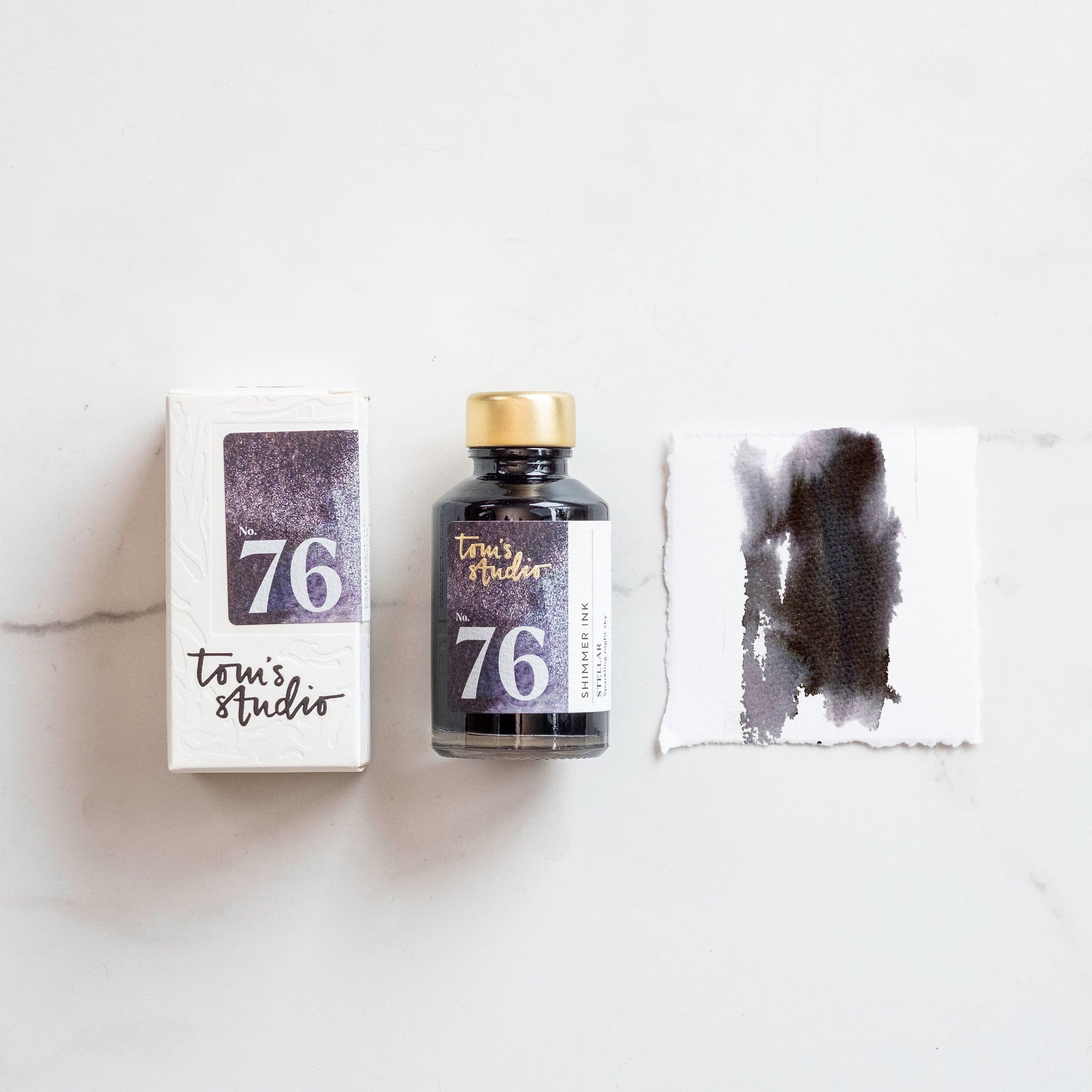 Tom's Studio Stellar Shimmer Fountain Pen Ink with two pens with inky goodness on paper with an ink swatch demonstrating the colour