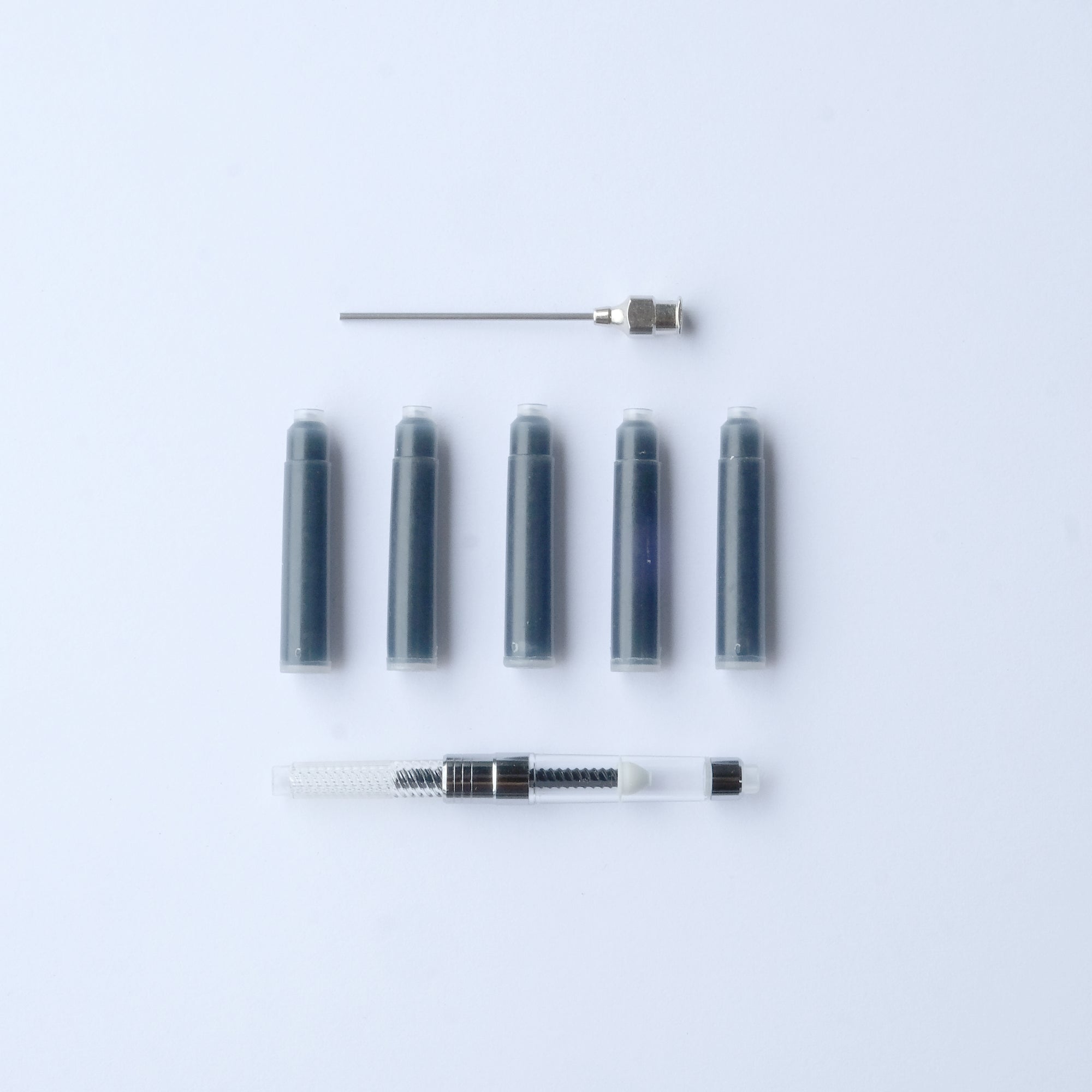 Five ink cartridges and an ink converter and syringe attachment displayed on a white plain background. 