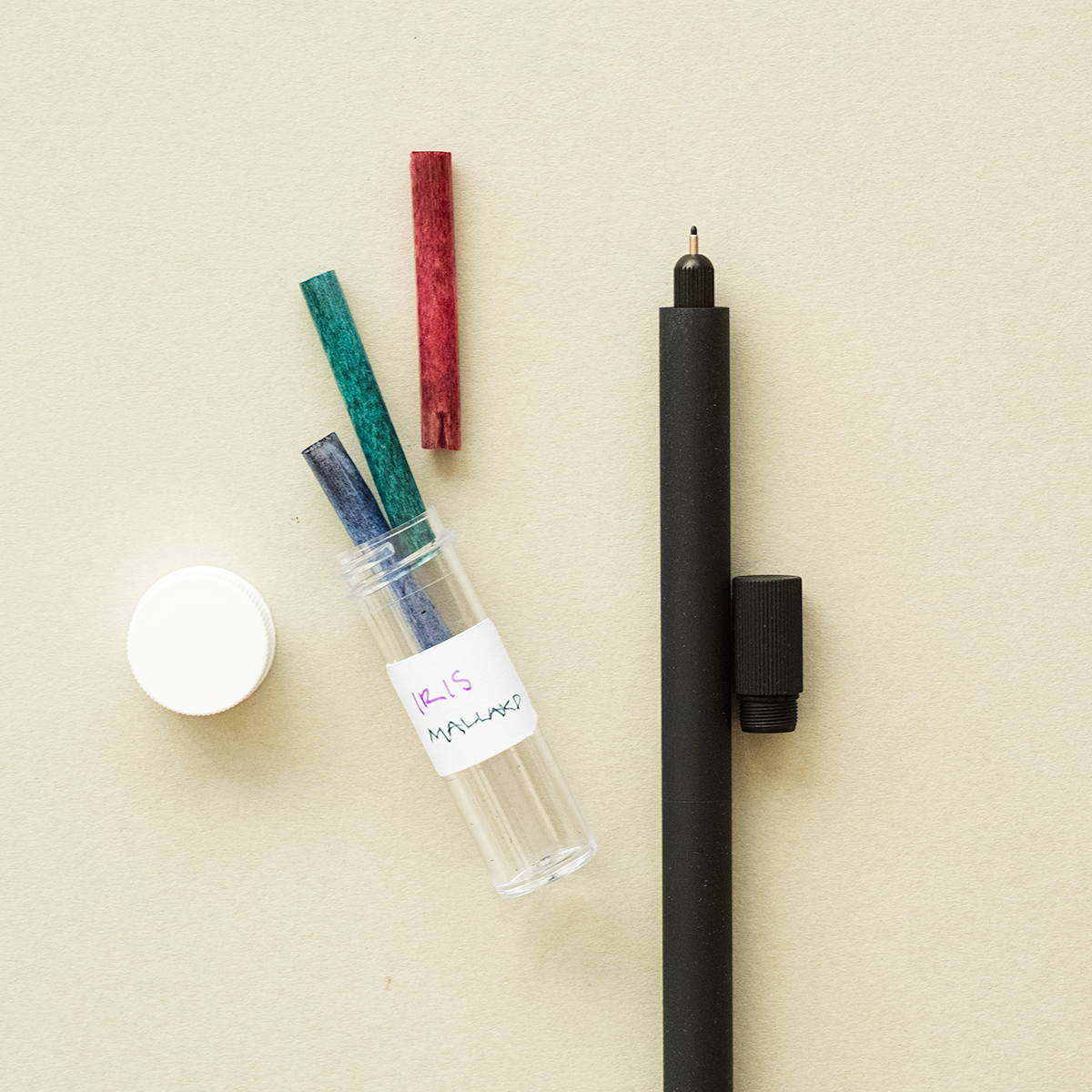 A Matte Black Lumos Duo and a Reservoir and Tip Container displayed on a light beige coloured background. The container has it's lid off and 3 ink reservoirs are coming out of the container that are colours with red, green and blue ink.